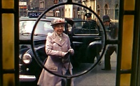 Film: Mrs Wilberforce seen through window in front door; black police car in background